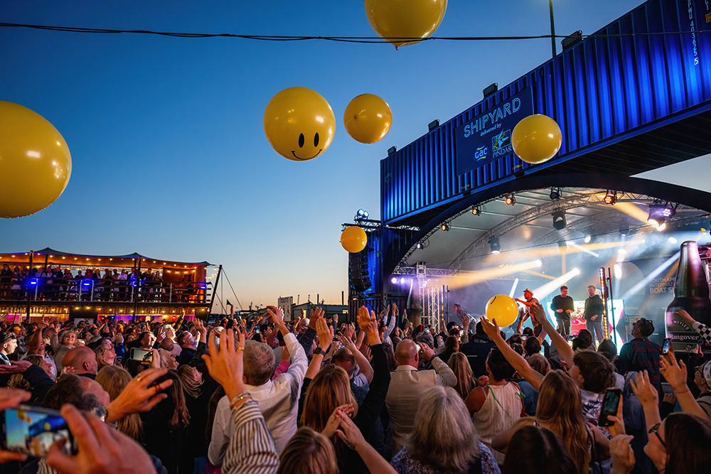 Crowds enjoy live music at Southampton Boat Show’s Shipyard stage, with yellow balloons and stage lights creating a festival atmosphere.