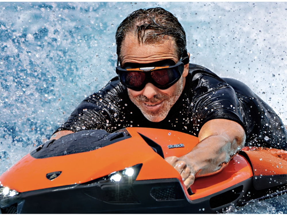 Man rides bright orange SEABOB SE63 by Lamborghini across blue water.