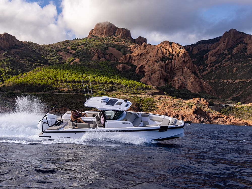Axopar boat with twin Mercury outboards cruising at speed along a rocky coastal landscape.