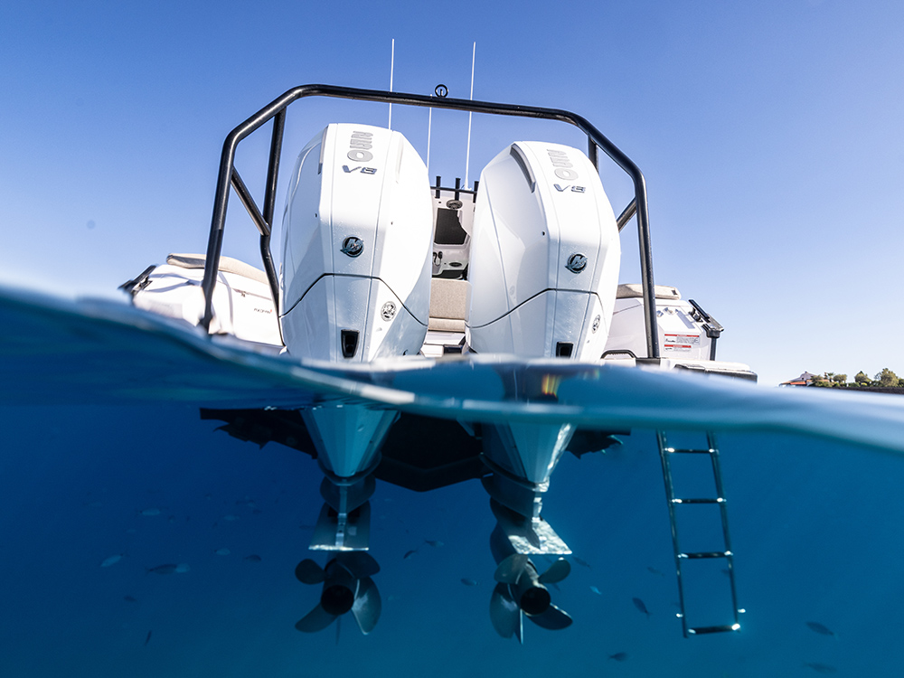 Twin white Mercury V8 outboard engines on an Axopar boat captured above and below the waterline in clear blue sea.