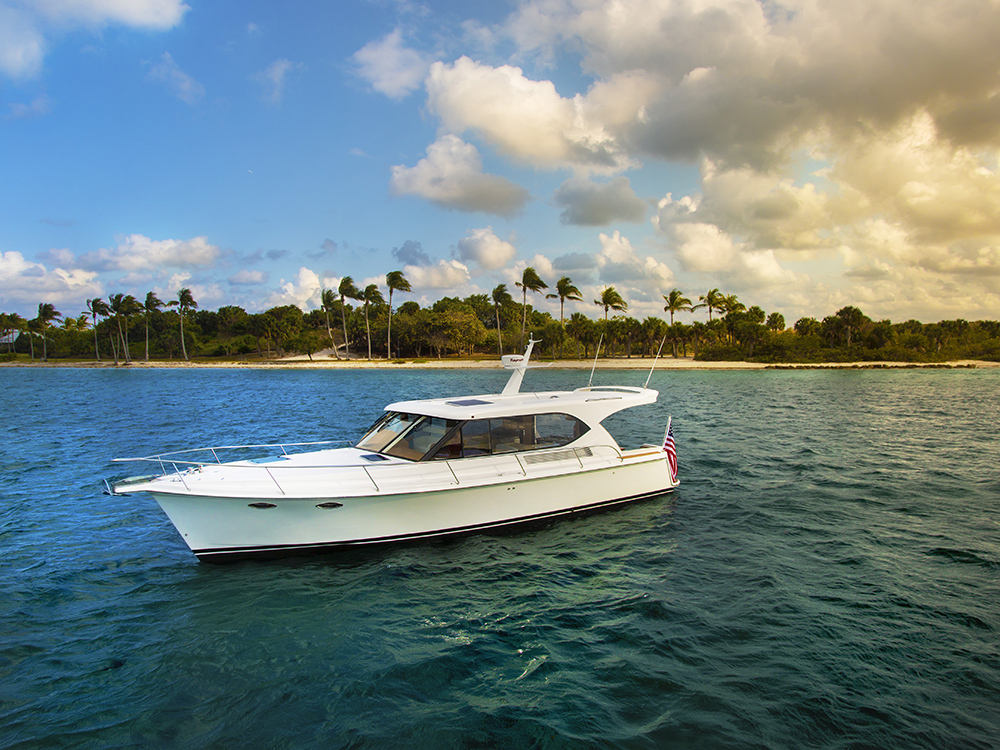 Hylas motor yacht cruising on blue water with tropical palm-lined shore in the background.