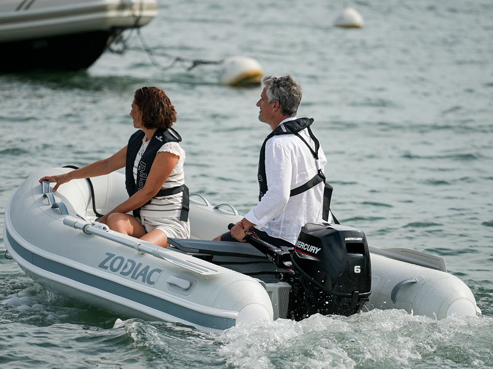 Couple cruising in a Zodiac inflatable boat powered by a Mercury 6HP EFI outboard on calm coastal waters.