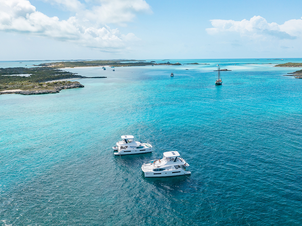Two power catamarans cruise in clear turquoise waters near small islands under a bright blue sky.