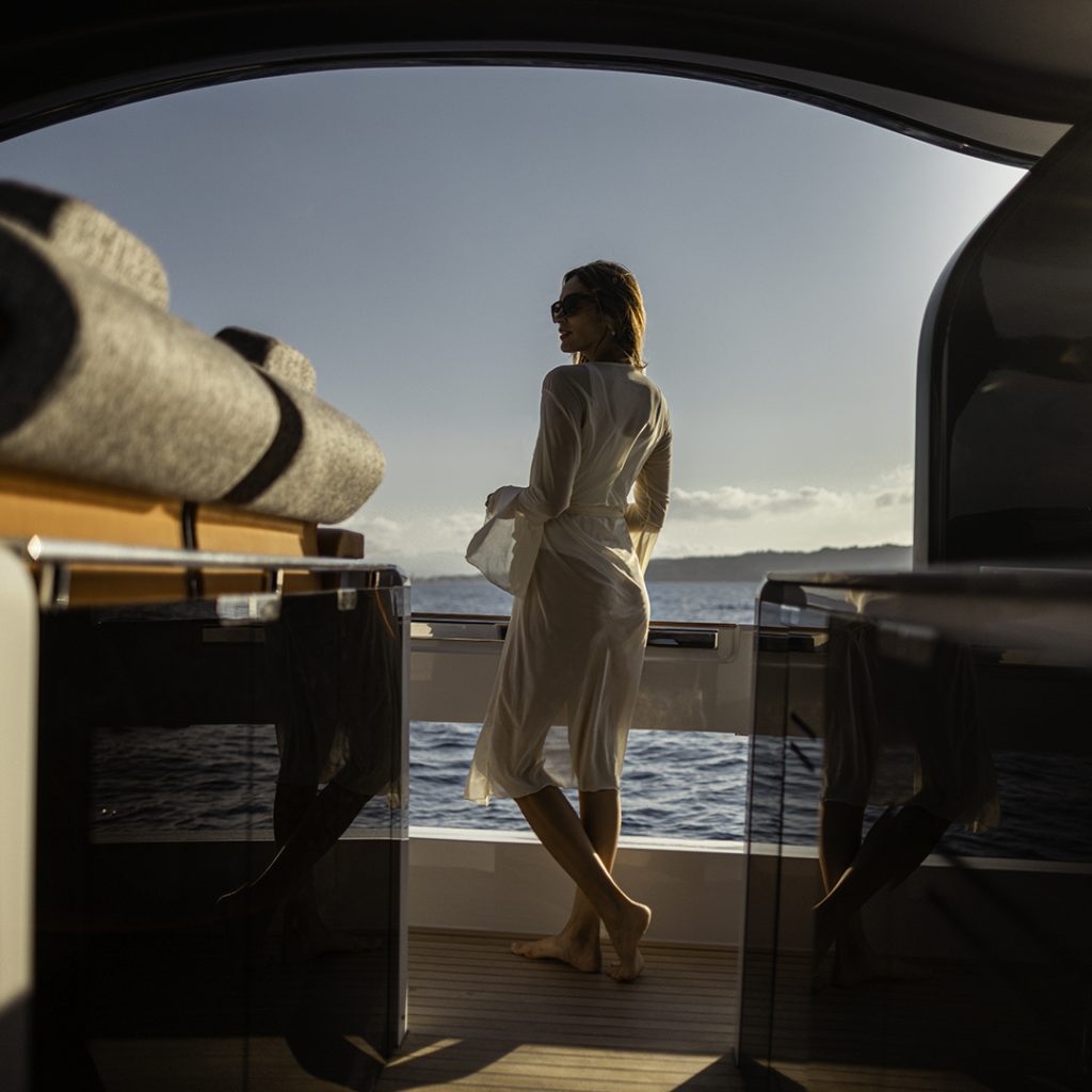 Woman standing at the stern of the Invictus TT550, gazing out over calm blue sea in evening light.