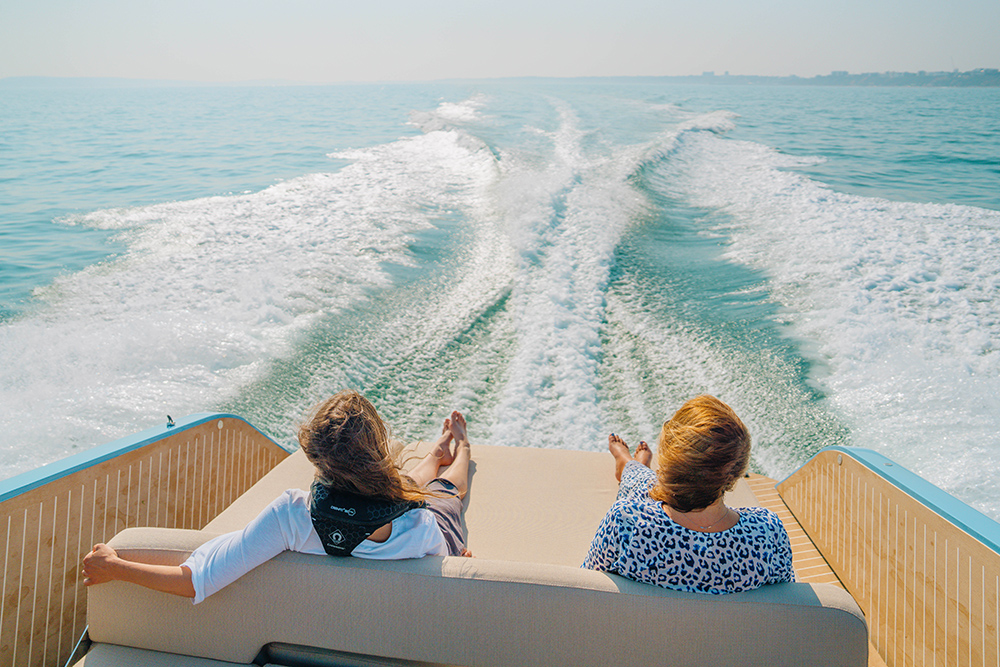 Two girls sat facing aft on sunbed of Bellini Astor 36 with wake in front of them