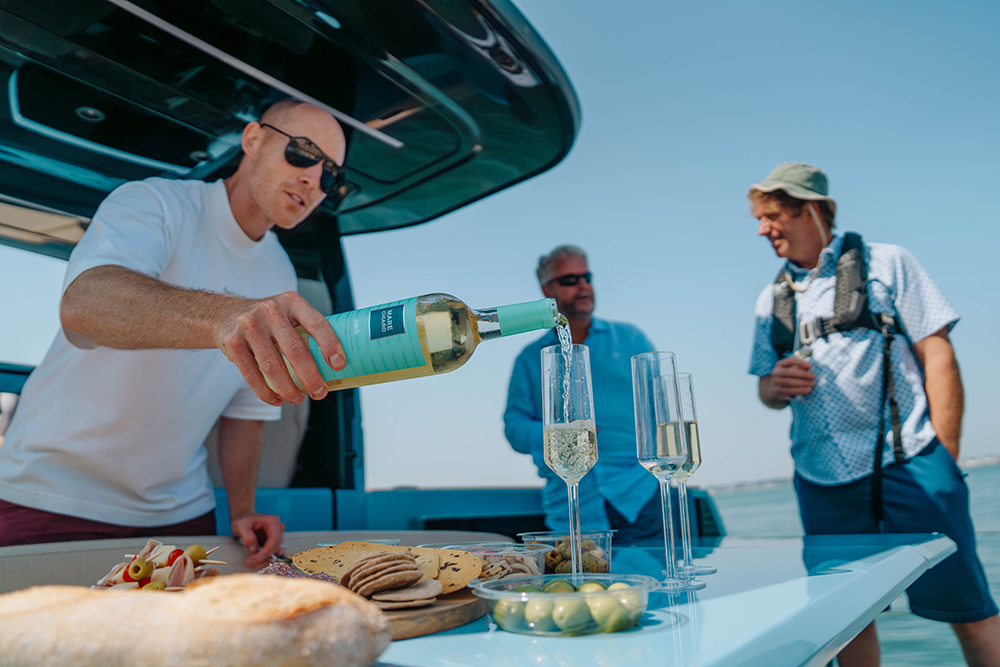 Man pouring white wine into 2 tall glasses onboard a boat
