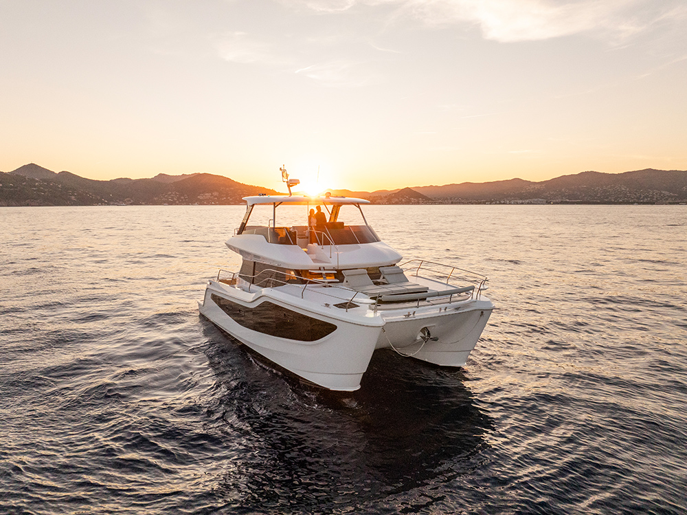 Aquila 46 Yacht cruising at sunset on calm coastal waters, showcasing its sleek twin-hull design and spacious flybridge.