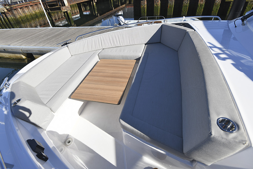 Forward deck seating area aboard Bavaria VIDA 33 with cushioned benches and teak table beside a pontoon.