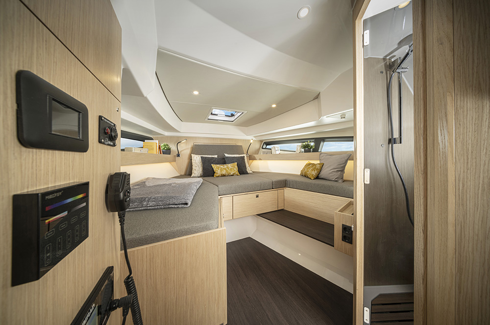Forward cabin aboard Bavaria VIDA 33 with double berth, soft lighting, and oak cabinetry featuring storage drawers.