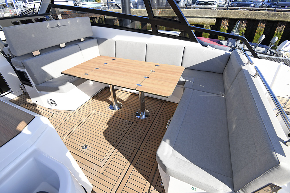 Spacious cockpit lounge aboard Bavaria VIDA 33 with L-shaped seating and teak dining table aboard a contemporary motor yacht in harbour.