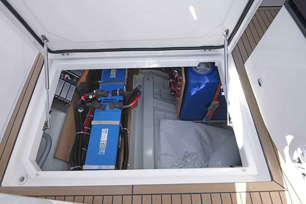 Underdeck storage compartment aboard Bavaria VIDA 33 showing neatly installed batteries, wiring, and equipment.