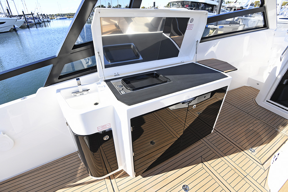 Cockpit wet bar on Bavaria VIDA 33 with sink, grill, and glossy black storage cabinets on teak decking.