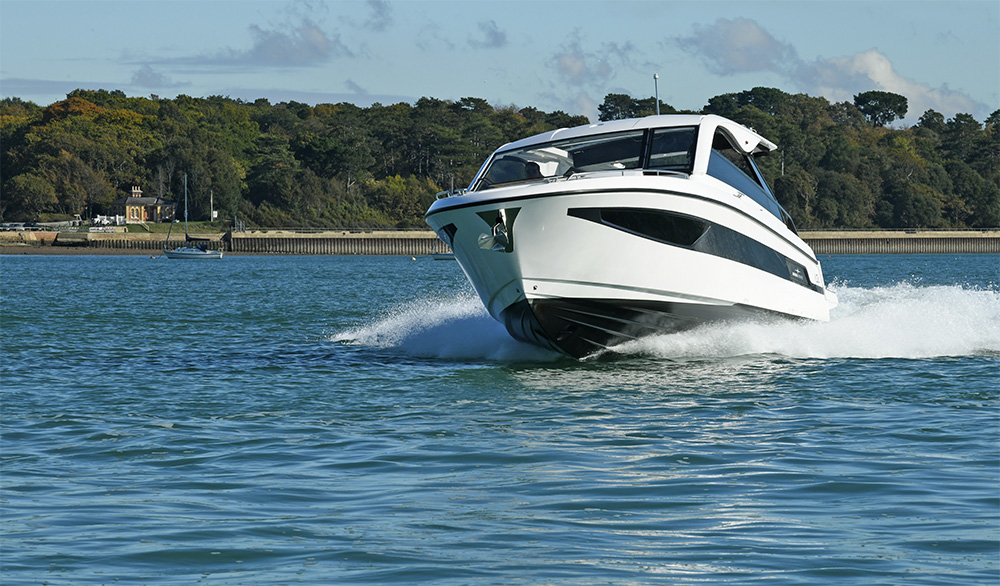 Bavaria VIDA 33 motor yacht cruising at speed in calm coastal waters with forested shoreline in the background.