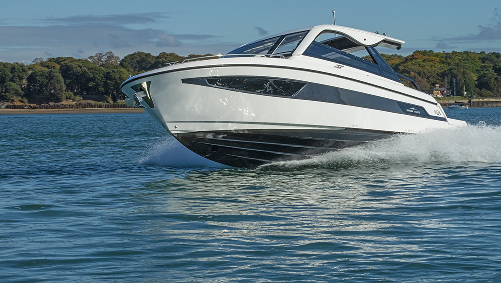 Bavaria VIDA 33 motor yacht cruising at speed in calm coastal waters with forested shoreline in the background.