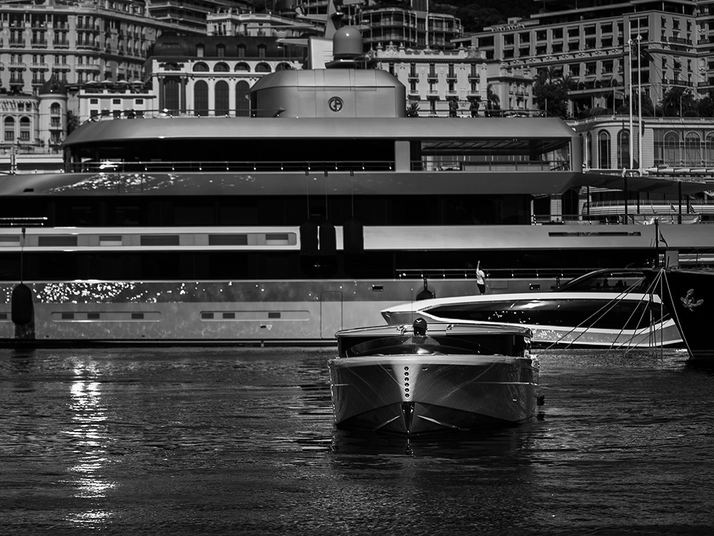 Sleek Falcon superyacht tender gliding in Monaco harbour with luxury yachts in the foreground and waterfront buildings in the background.