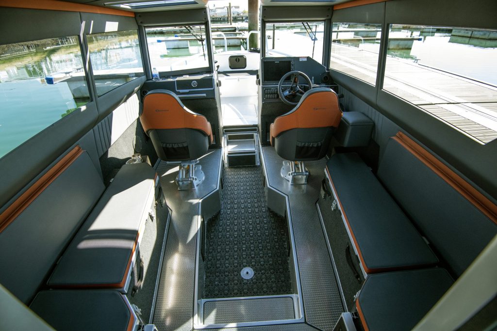 Ockelbo B25 CAB spacious cabin with twin helm seats and side bench seating, docked beside marina pontoons.