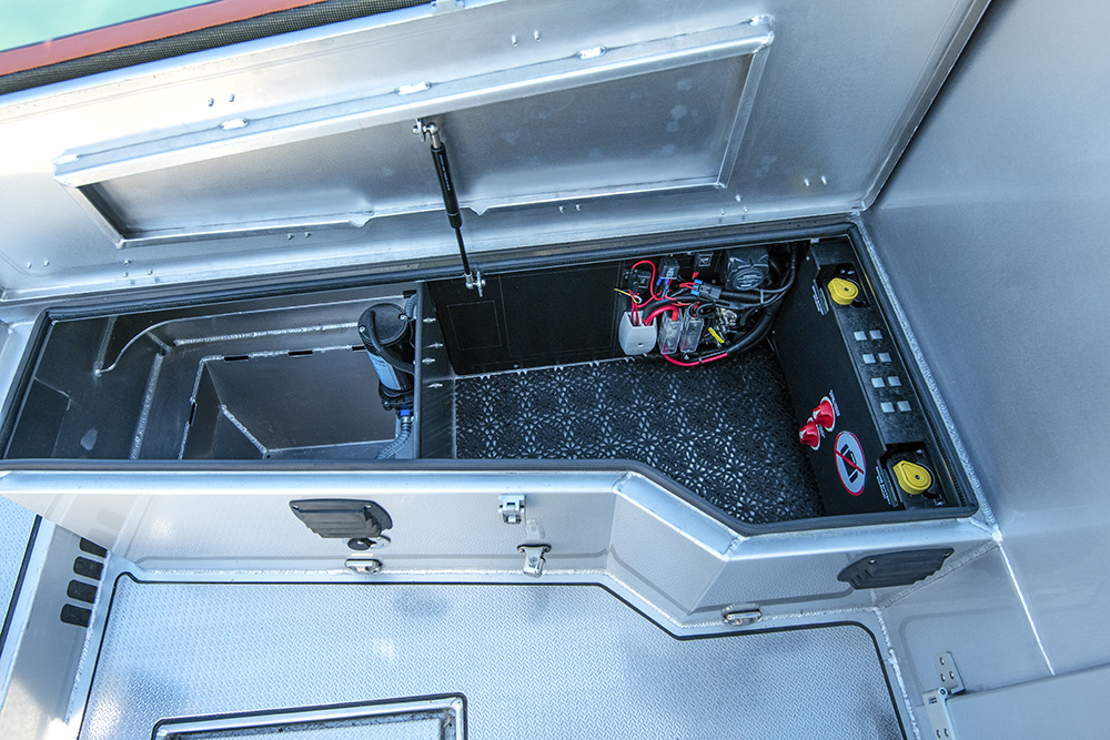 Open deck locker on Ockelbo B25 CAB showing battery switches, wiring, and storage compartments with non-slip flooring.