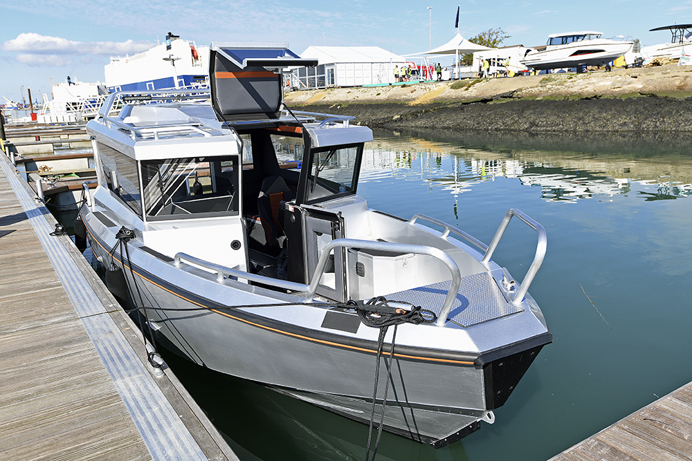 Ockelbo B25 CAB moored beside pontoon, featuring walkaround deck, forward rails and open wheelhouse door in marina setting.