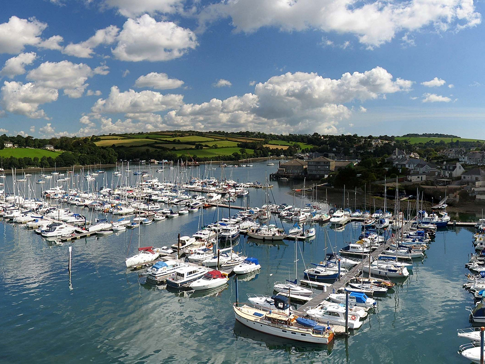Boats and yachts moored at Falmouth Marina in calm water under a bright, partly cloudy, sky.
