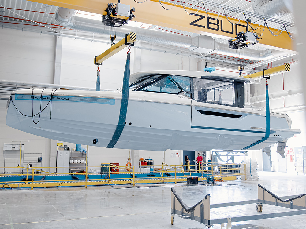 Saxdor yacht suspended by crane inside modern Finnish shipyard facility.