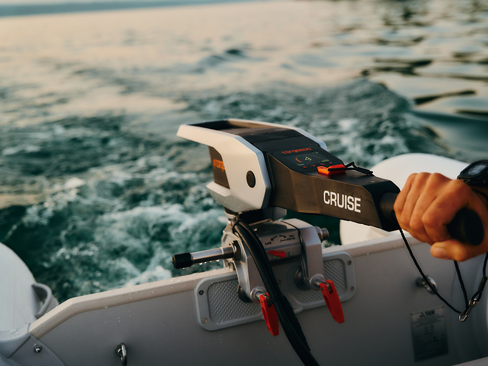 Torqeedo Cruise electric outboard in use on a small boat, showing tiller controls as it powers across calm open water.