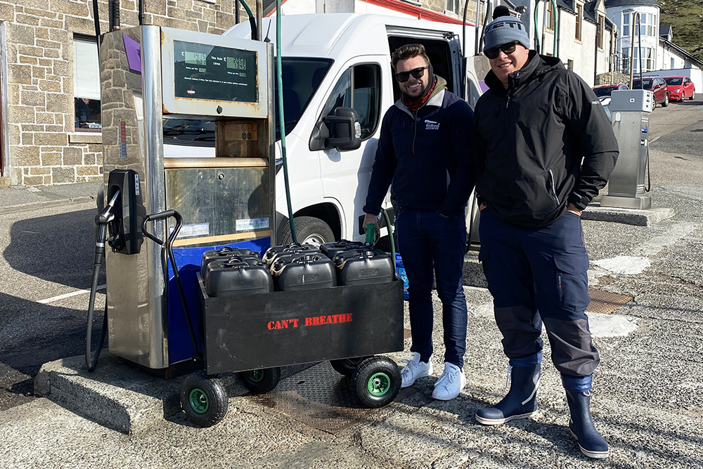 Two team members refuelling jerry cans at a fuel pump.