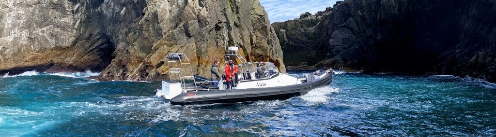 RIB touring through a narrow rocky channel, turquoise water swirling around steep cliffs.
