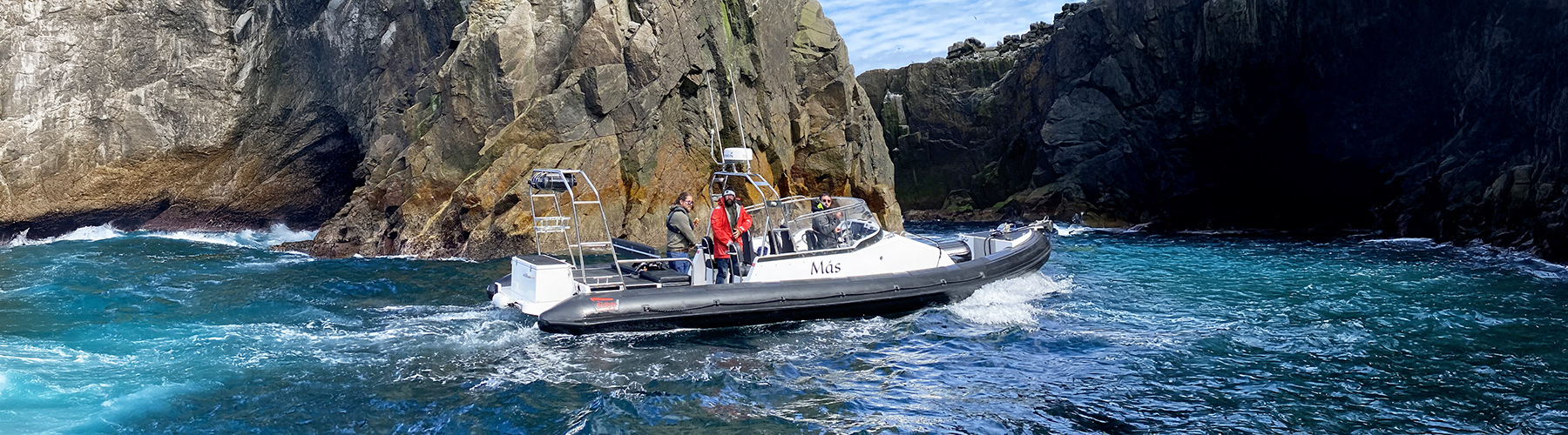 RIB touring through a narrow rocky channel, turquoise water swirling around steep cliffs.