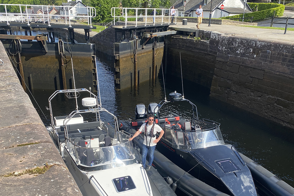 Two RIBs inside a canal lock, with lock gates and waterside buildings in the background.