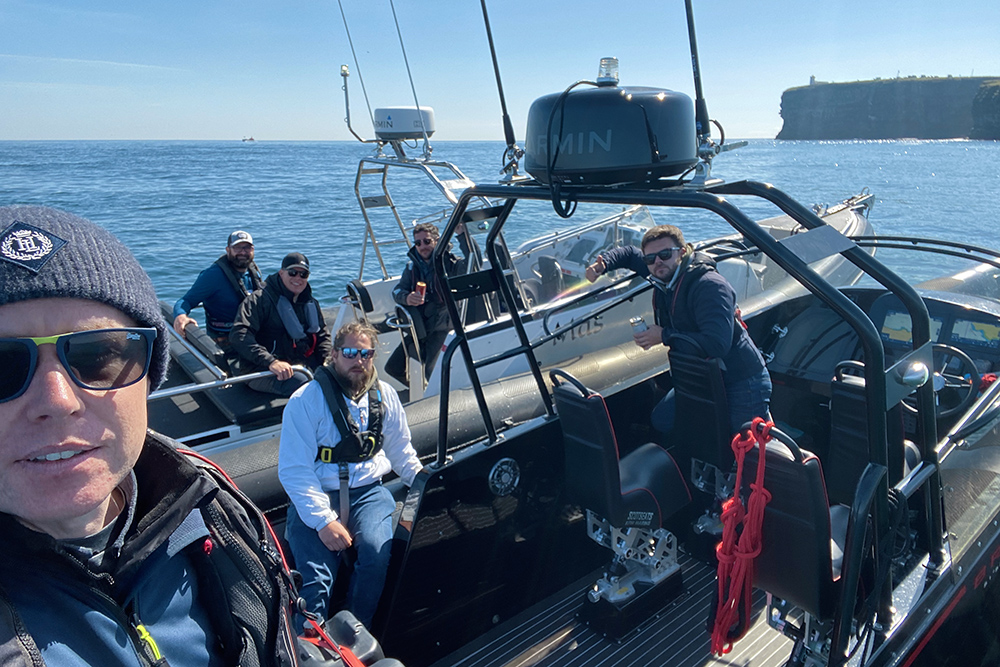 Team members relaxing on two RIBs on calm open water, with clear skies.