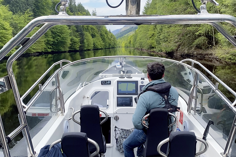 Team member navigating a RIB along a calm tree-lined river, in still water.