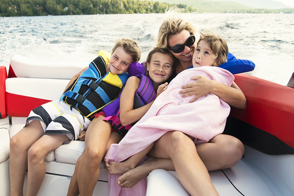 Mother with three children in lifejackets, one wrapped in towel on aft bench of boat