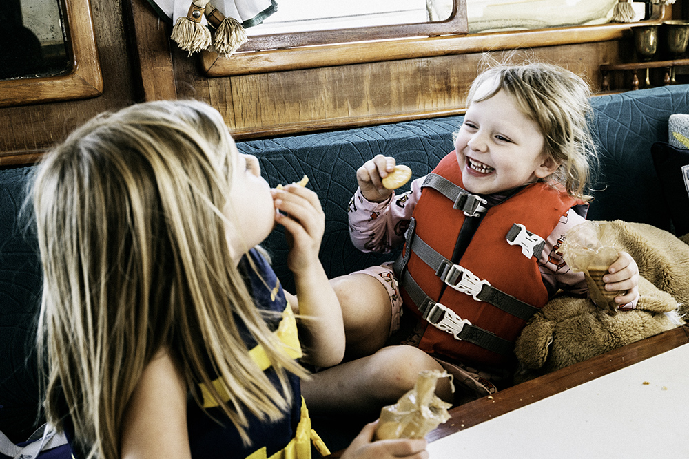 Two children in lifejackets eating snacks onboard classic boat