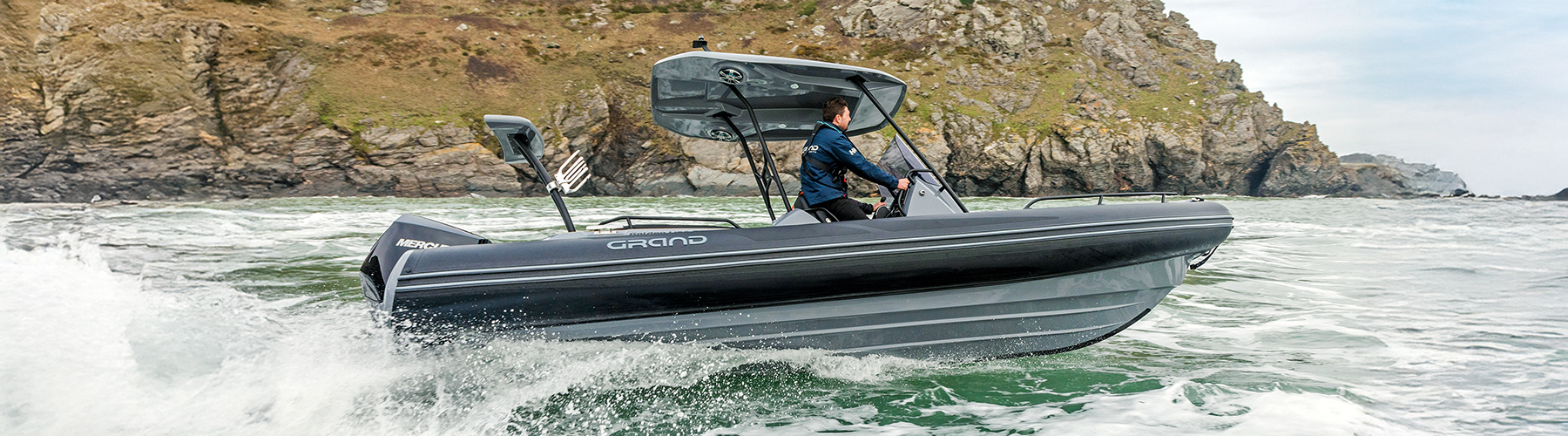 Grand 680 RIB underway at sea with cliffs behind