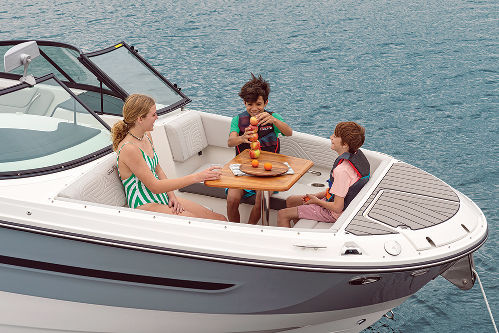 Three children sat in a bowrider boat stacking apples on the dining table