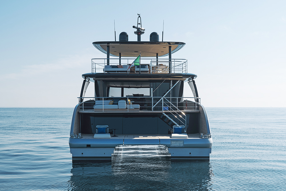 Stern view of a Bluegame luxury motor yacht at rest, showcasing wide terraces, steps to the water and open lounge areas on a calm sea.
