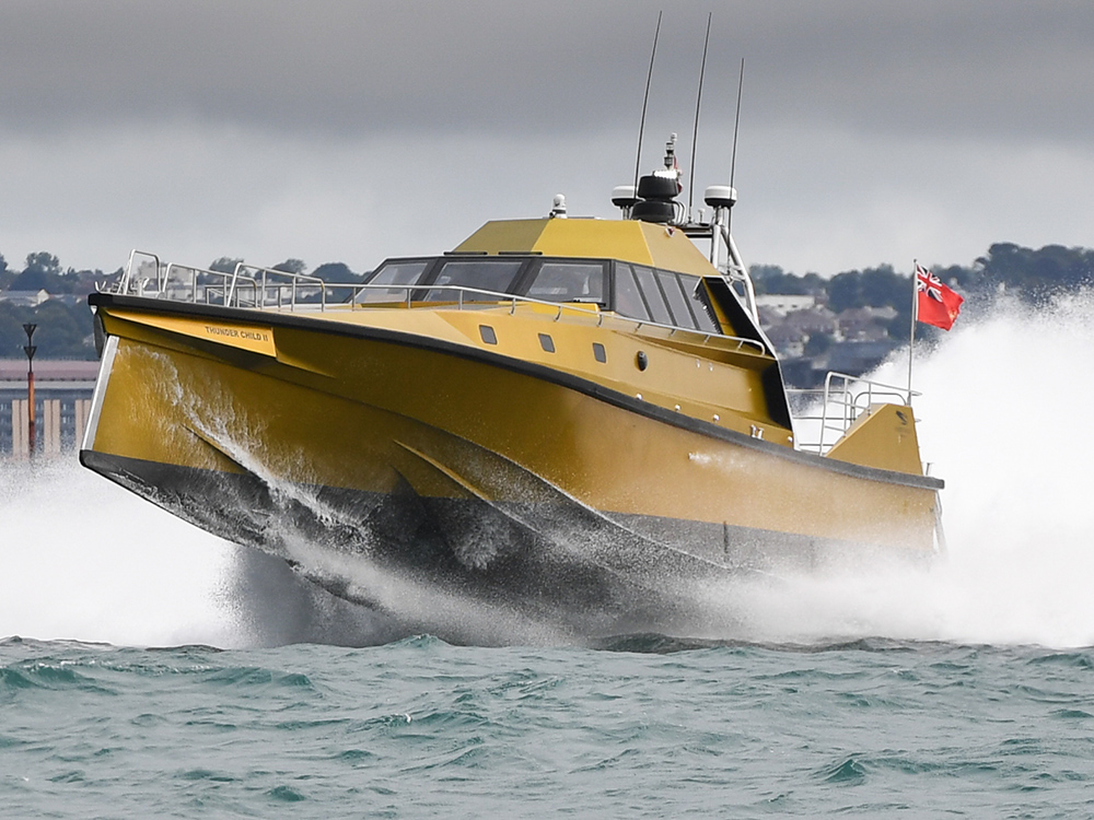 Thunder Child II driving at speed in choppy seas, lifting clear of the water as spray breaks around its yellow trimaran hull.