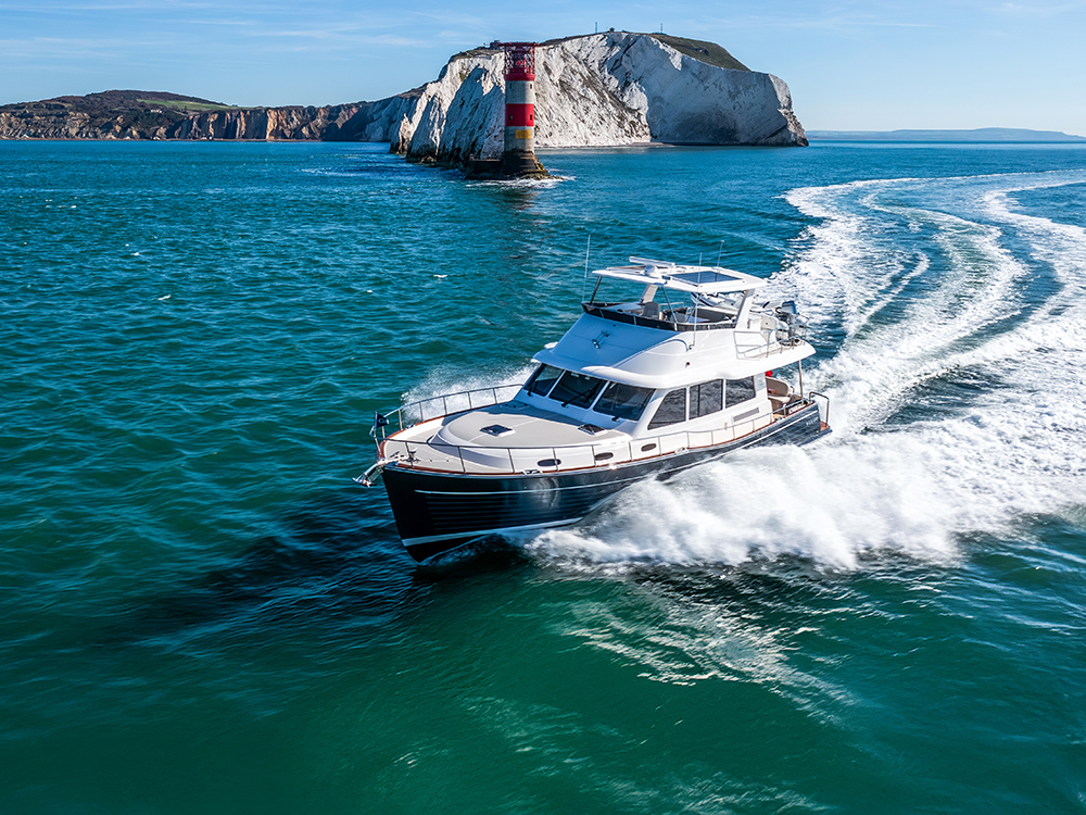 Grand Banks 54 cruising at speed past the Needles lighthouse in clear blue waters under bright skies.