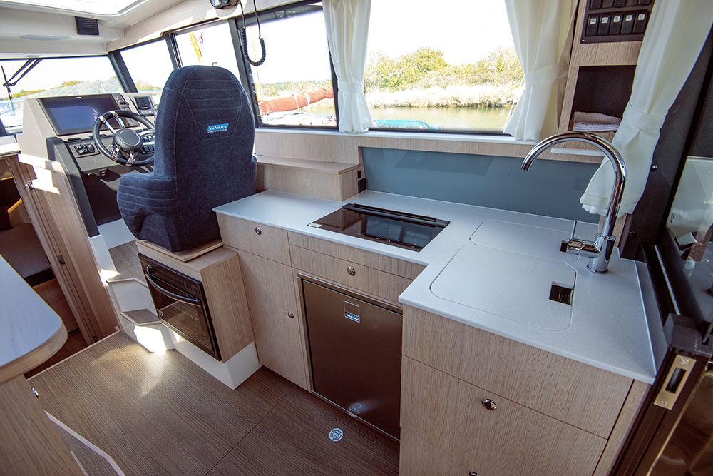 Galley to Viknes 10 in clean light wooden finish positioned behind helm seat featuring lots of drawers and storage