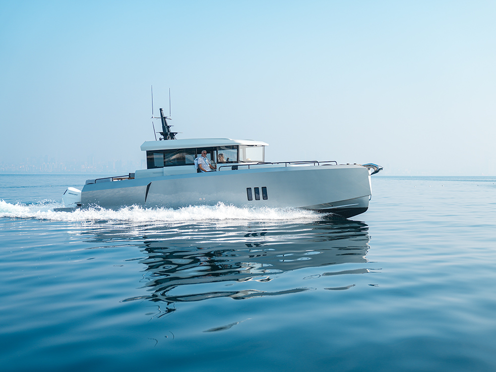 XO EXPLR 44 cruising at speed on calm blue water with two people at the helm.