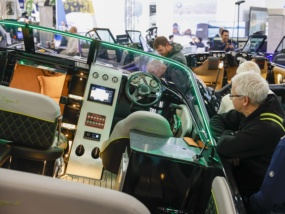 Visitors inspect a motorboat interior at boot Düsseldorf, viewing the helm, seating, cabin space, and illuminated dashboard features.