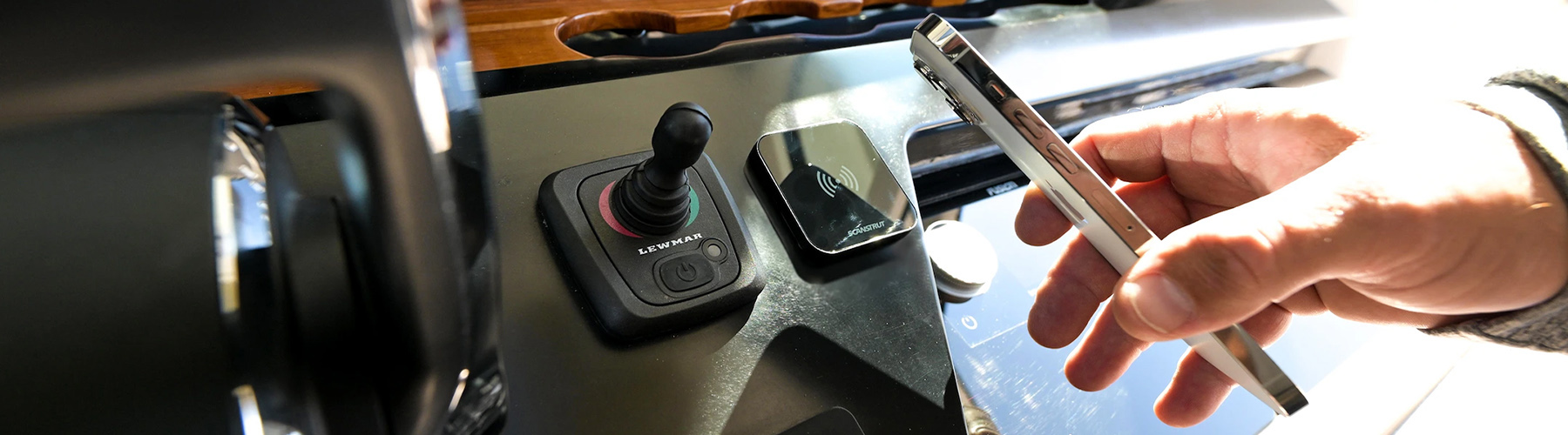 Hand holding mobile phone towards Scanstrut Utlra wireless charger on boat dash