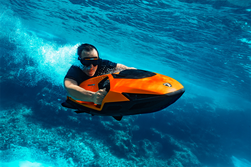 Man holding on to SEABOB personal sea scooter at speed through a bright blue sea