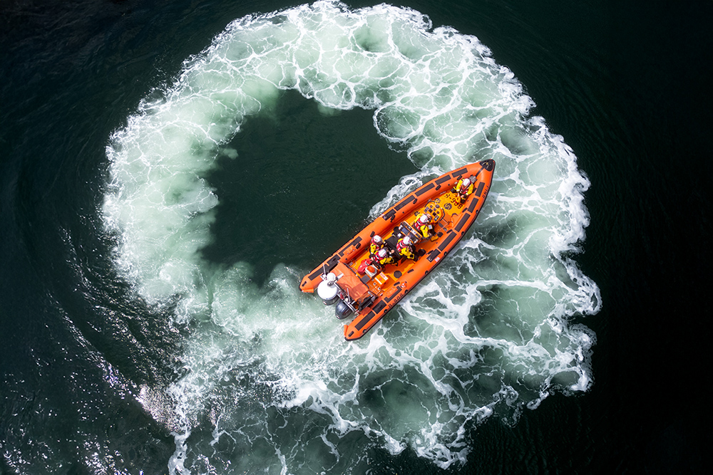 Aerial view of RNLI lifeboat, creating circular wake during on-water demonstration at Plymouth Boat Fest.