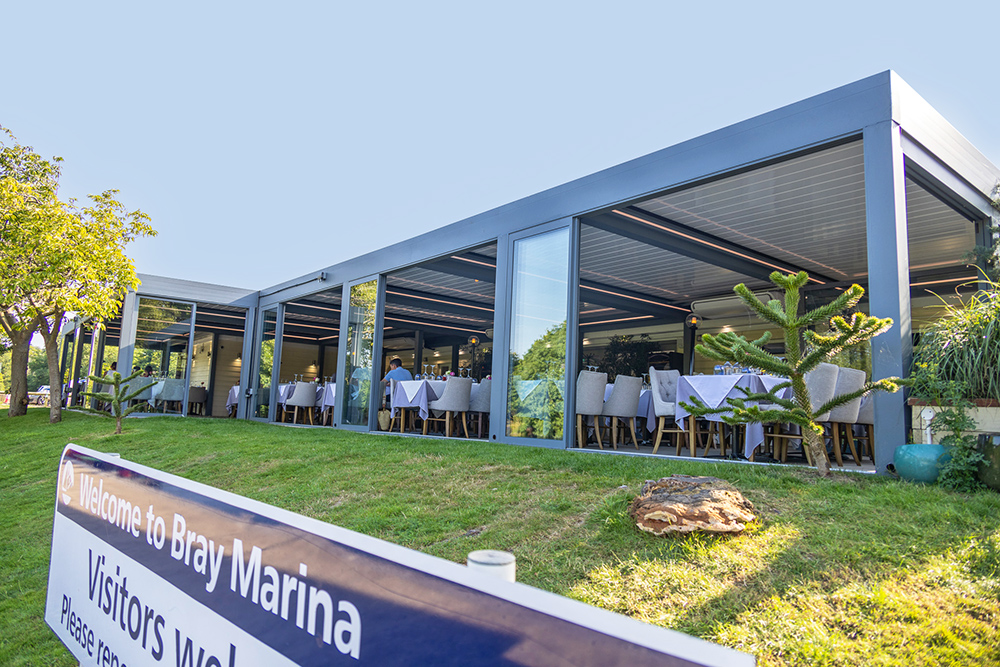 Modern glass-fronted marina restaurant at Bray Marina with outdoor seating overlooking landscaped grounds and waterside setting.