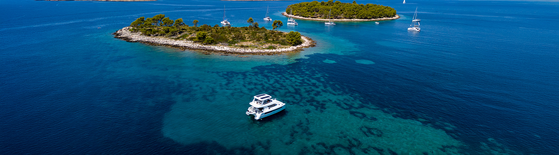The Moorings power catamaran moored on turquoise sea with forested islands and sailing yachts nearby