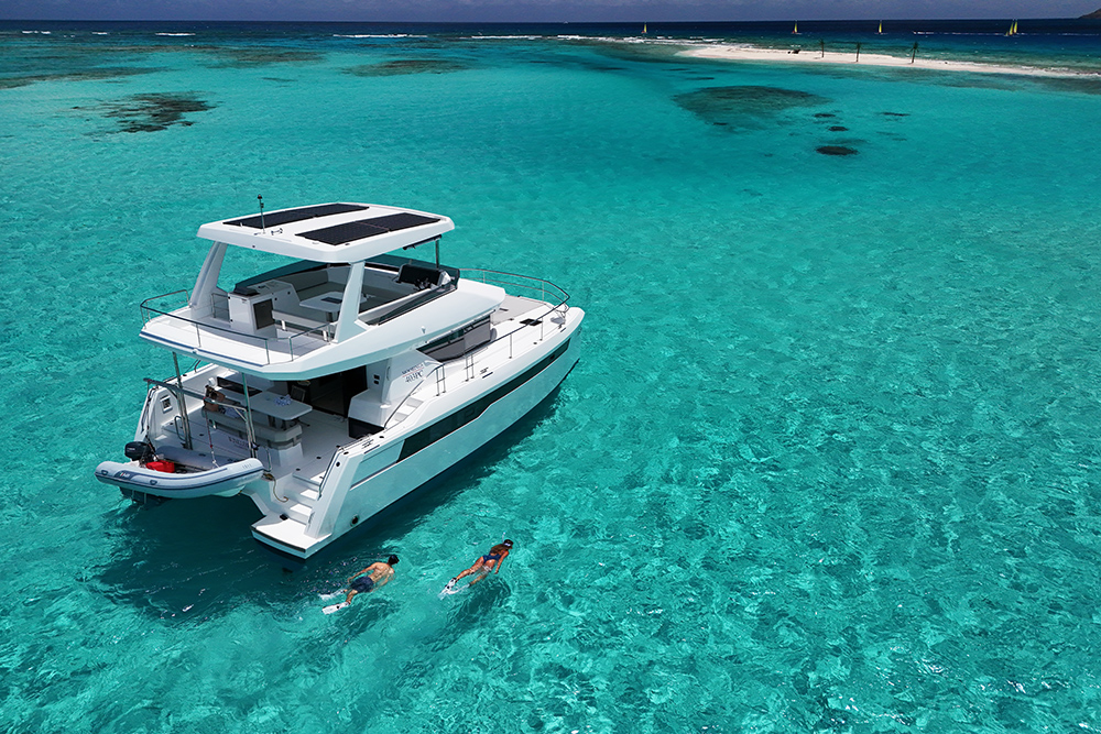 Couple swimming in turquoise waters off a power catamaran
