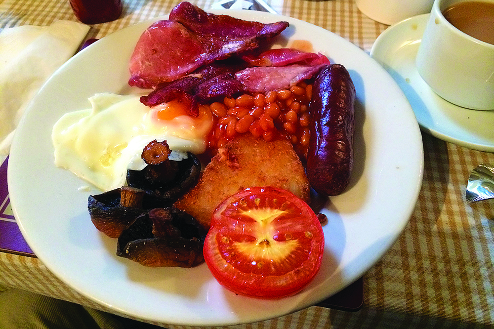 Full English breakfast with bacon, sausage, fried egg, beans, mushrooms, hash brown and tomato, served with tea.