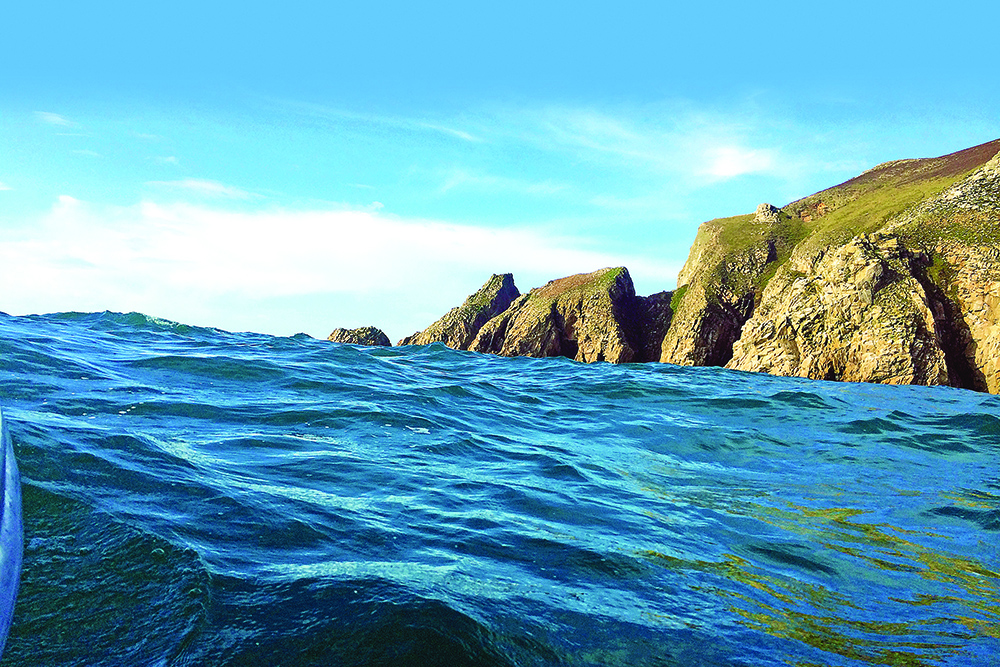 Ocean swells rolling close to rugged coastal cliffs under clear blue sky.