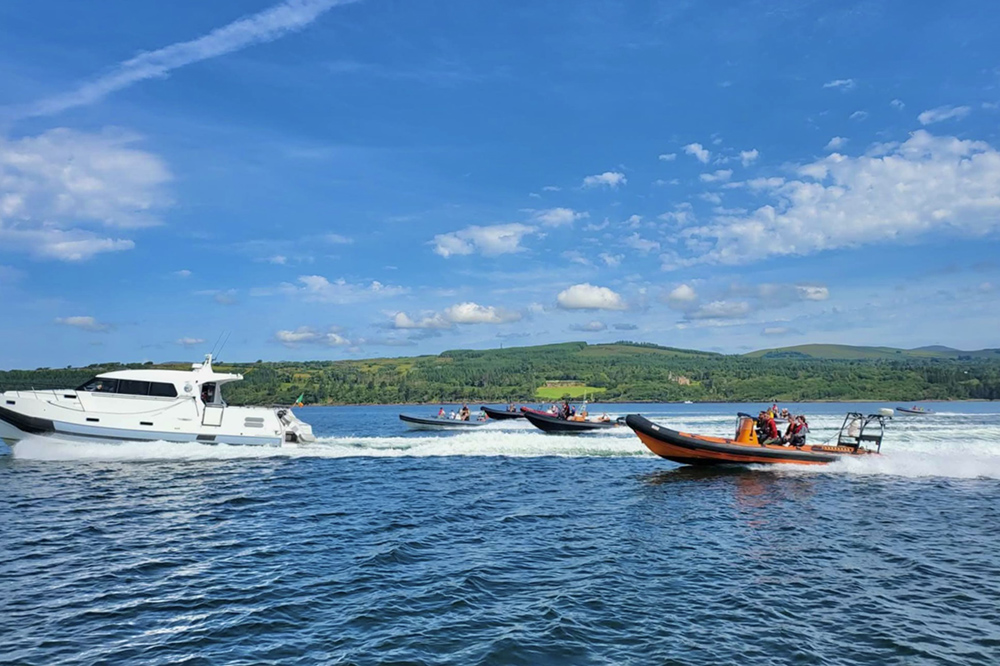 Mixed fleet of powerboats and RIBs cruising together across Kenmare Bay during the Bull Run for Fun, with green Kerry hills under clear summer skies.